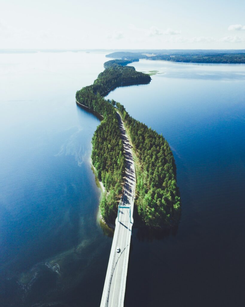 Värillisessä ilmakuvassa maantie kiemurtelee ohutta metsäistä kaistaletta, jonka molemmin puolin avautuu järvenselkä.